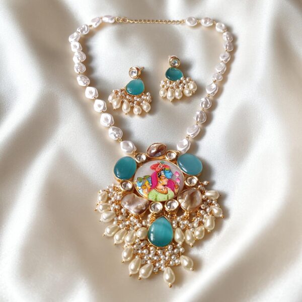 Turquoise Monalisa stone necklace with a Radha Krishna painting on a milky white centre stone, pearl detailing, kundan-inspired work and matching earrings on white satin.
