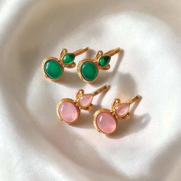 Two pairs of gold plated Bugadi earrings with green and magenta Monalisa stones arranged on an ivory satin background.