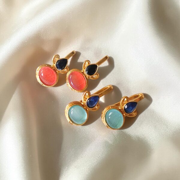 Two pairs of gold plated Bugadi earrings with pink and sky blue Monalisa stones arranged on an ivory satin background.