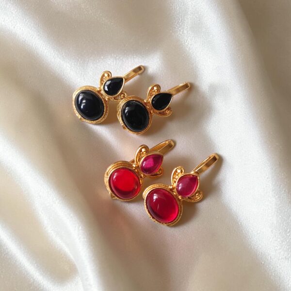 Two pairs of gold-plated Bugadi earrings with black and ruby red Monalisa stones arranged on ivory satin.